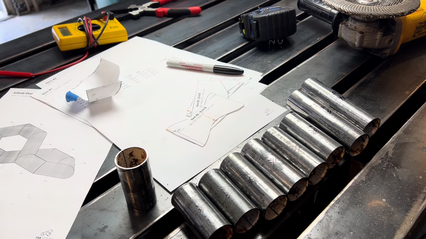 Printed miter templates and cut tube pieces laid out on the workbench alongside the build packet drawings.