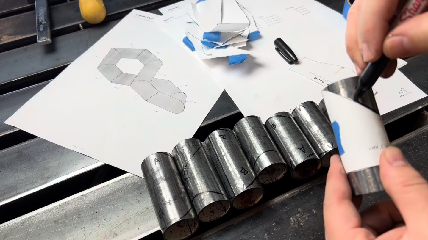 Hands tracing the miter cut line from a printed template wrapped around a tube, with the assembly drawing visible in the background.