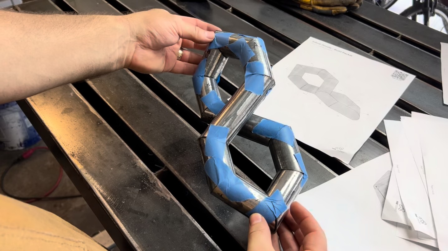 The cut tube pieces assembled and taped together in a test fit, confirming tight joint contact before welding. The FitUp build packet is visible in the background.