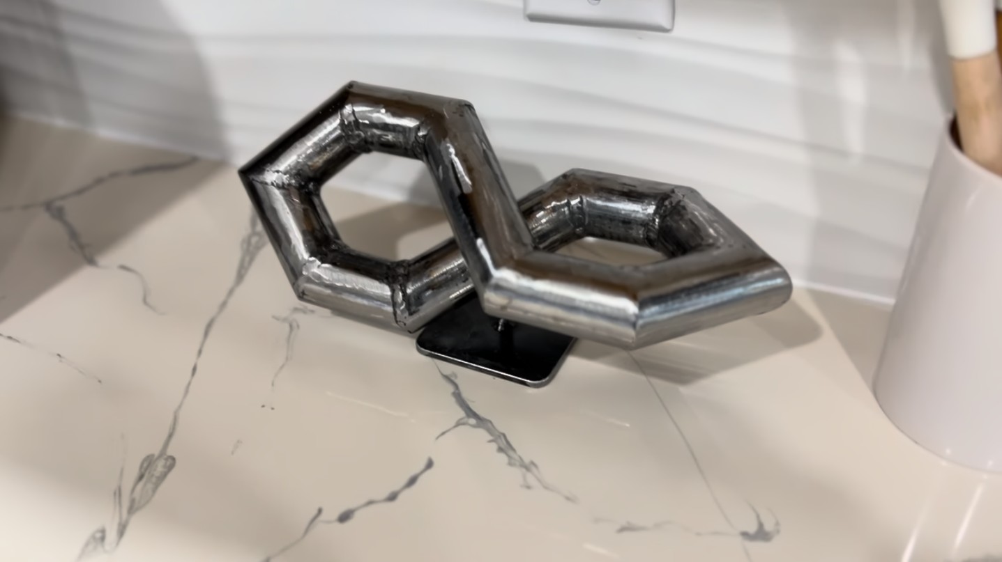 The finished welded infinity tube sculpture, polished and displayed on a marble surface.